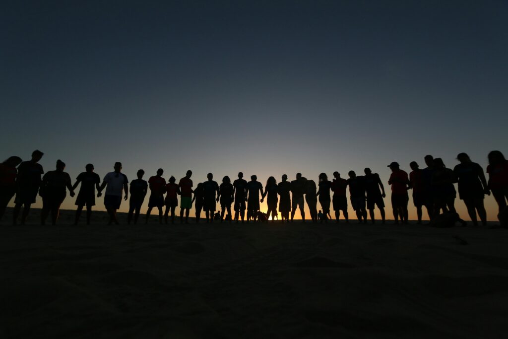 A large group holding hands as silhouettes during sunset, symbolizing unity and friendship.