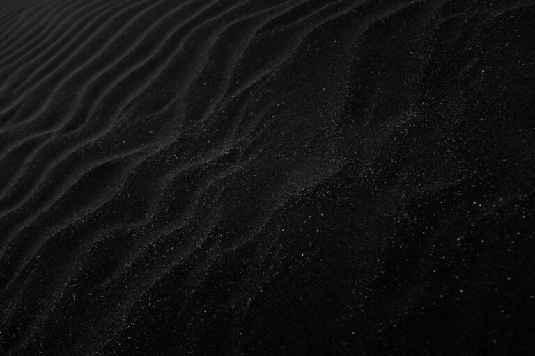 Textured black sand with ripples resembling dunes, creating a dark, abstract aesthetic.